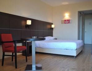A hotel room with a bed, a desk with a chair, and two wall-mounted lamps. - Belle Helene (East Mani)