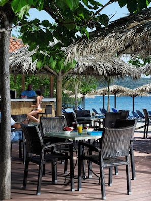 An outdoor seating area with wicker chairs and tables, a thatched roof, and a view of the sea. - Belle Helene (East Mani)
