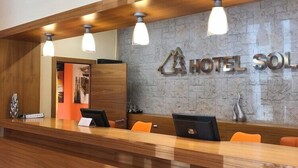 Un mostrador de recepción de hotel con diseño moderno, que cuenta con una encimera de madera, tres lámparas colgantes y una pared de piedra con el nombre del hotel.