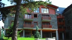 Un edificio de varios pisos con balcones, fachada de piedra y un área de entrada pavimentada.