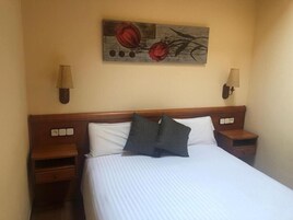 Habitación de hotel con una cama grande, dos mesitas de noche, un cuadro colgado en la pared y dos apliques.