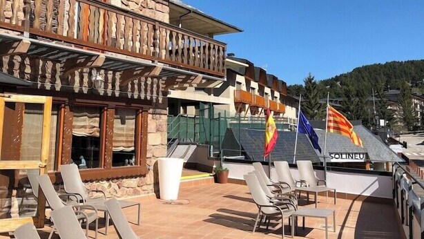 Un edificio con varios balcones, mobiliario exterior y banderas.