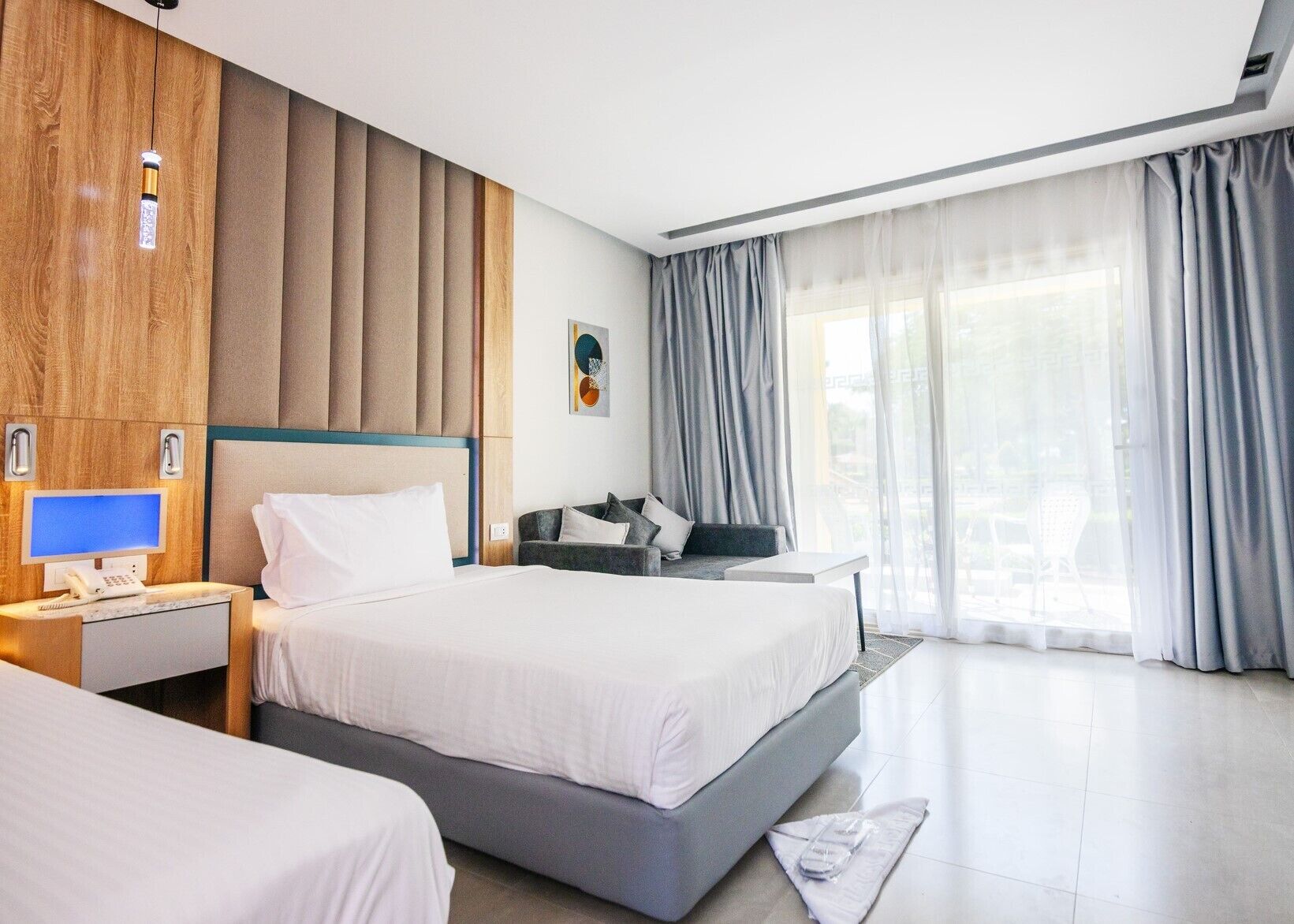 Een hotelkamer met een groot bed, een bureau met een computer, een stoel en een raam met gordijnen.