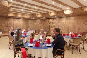 A restaurant with round tables, red napkins, and wooden wall carvings. - Hotel Titanic Beach Spa And Aqua Park (Hurghada)