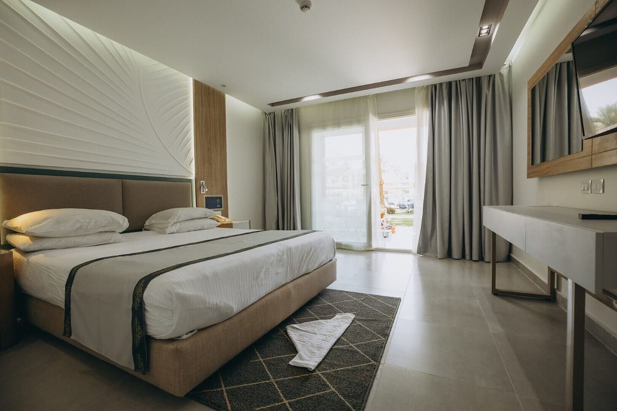 Quarto de hotel moderno com uma cama grande, uma mesa de cabeceira, televisão de tela plana e porta de vidro deslizante para o exterior.