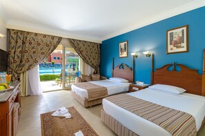 A hotel room with two beds, a desk with a chair, a TV, and a view of a pool and buildings outside. - Hotel Titanic Beach Spa And Aqua Park (Hurghada)