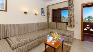 A room with a striped sofa, a wooden table with drinks, and a window with curtains. - Hotel Titanic Beach Spa And Aqua Park (Hurghada)