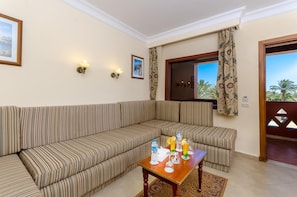A room with a striped sofa, a wooden table with drinks, and a window with curtains. - Hotel Titanic Beach Spa And Aqua Park (Hurghada)