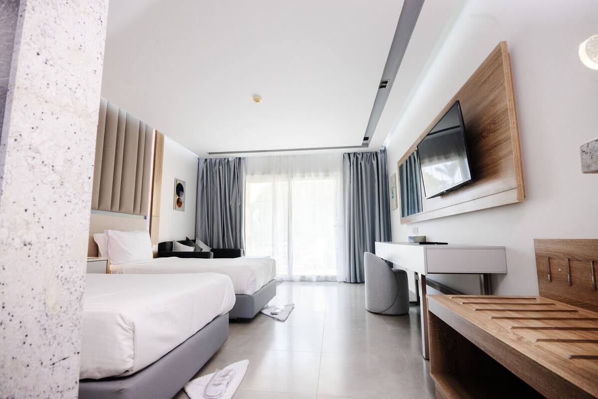 Quarto de hotel moderno com cama, escrivaninha, poltrona, televisão e banheiro.