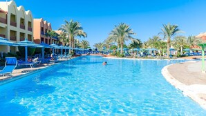 A large swimming pool with lounge chairs and umbrellas, surrounded by palm trees and hotel buildings. - Hotel Titanic Beach Spa And Aqua Park (Hurghada)