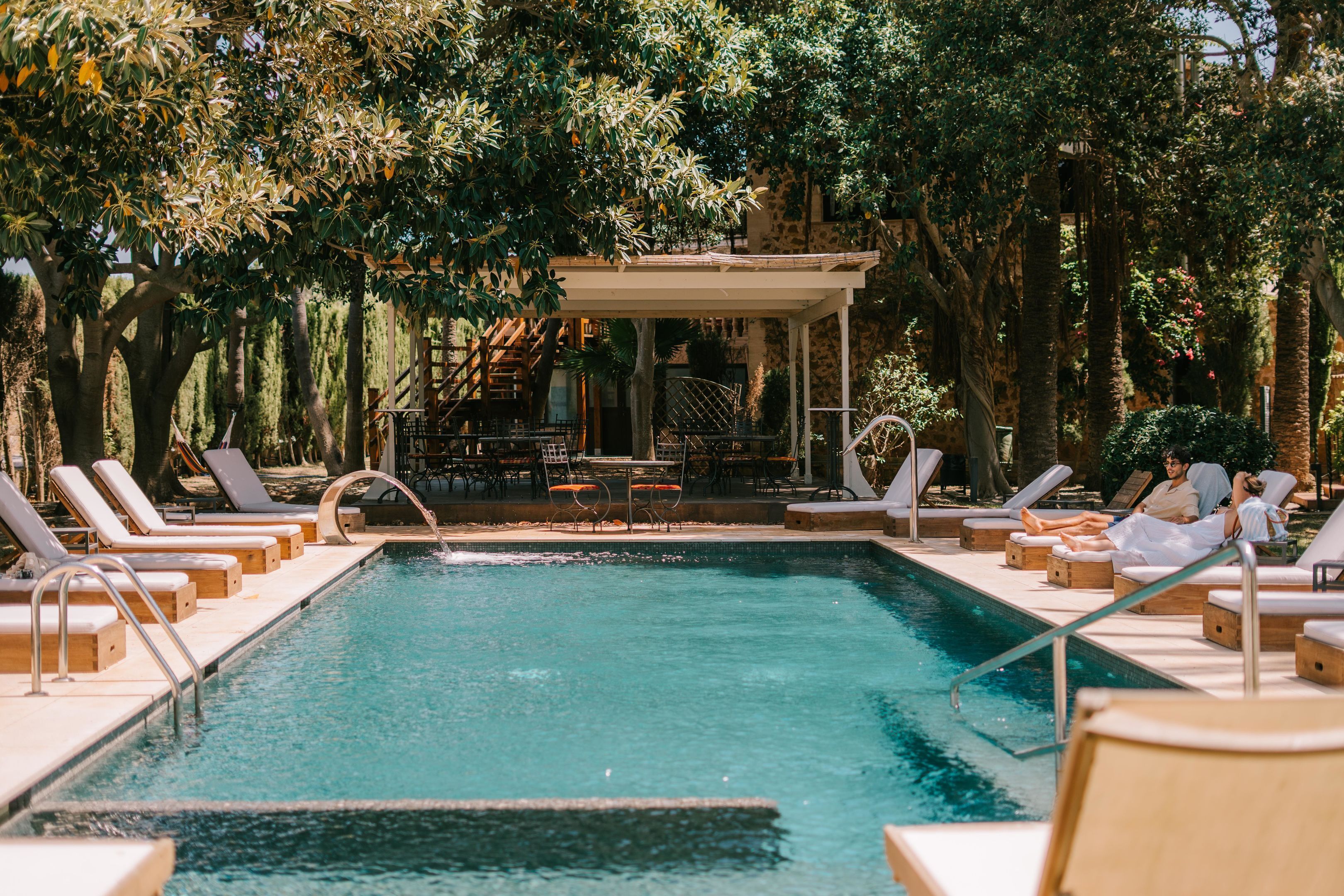 Area piscina con sedie a sdraio e una zona relax coperta, immersa nel verde.