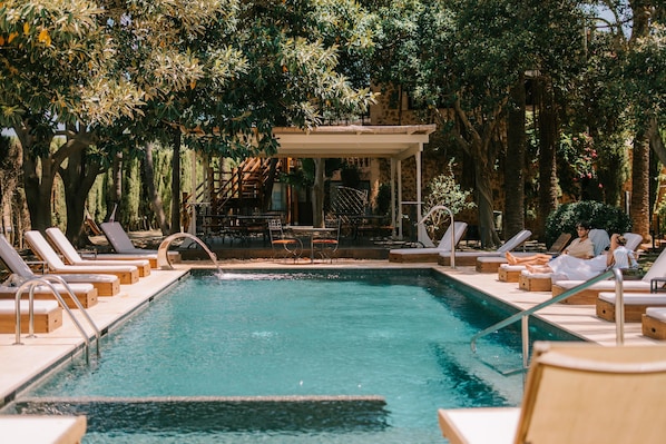 A pool area with lounge chairs and a covered seating area surrounded by trees.