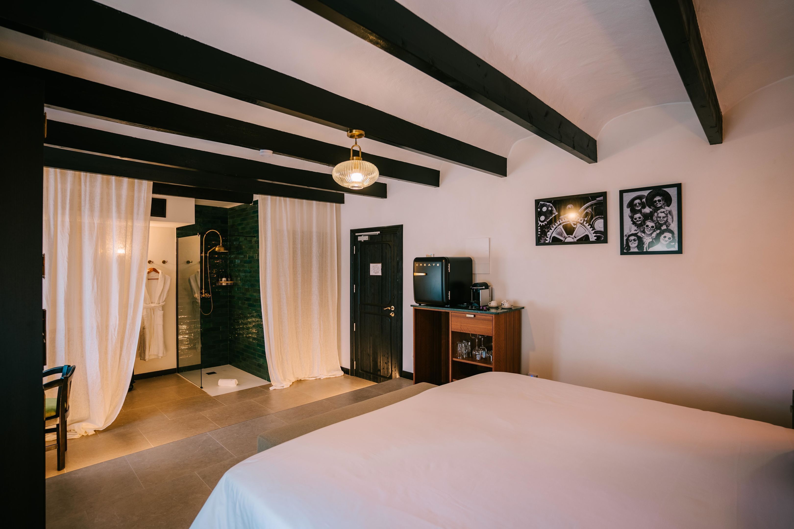A hotel room with a bed, a shower area, a wooden cabinet, and artwork on the wall.