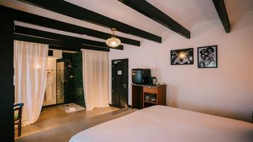 A hotel room with a bed, a shower area, a wooden cabinet, and artwork on the wall.