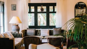 A cozy living room with a sofa, armchairs, a lamp, and a large window with curtains.