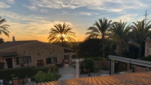 A stone building with a tiled roof, surrounded by palm trees and a sunset in the background.