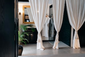 A room with a large mirror, white curtains, a potted plant, and a robe hanging on a rack.