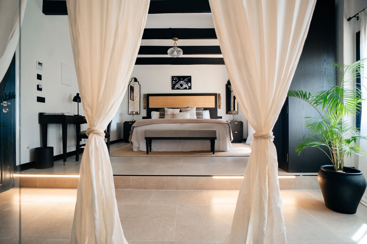 Een moderne slaapkamer met een groot bed, een hoofdbord met een spiegel en een potplant.