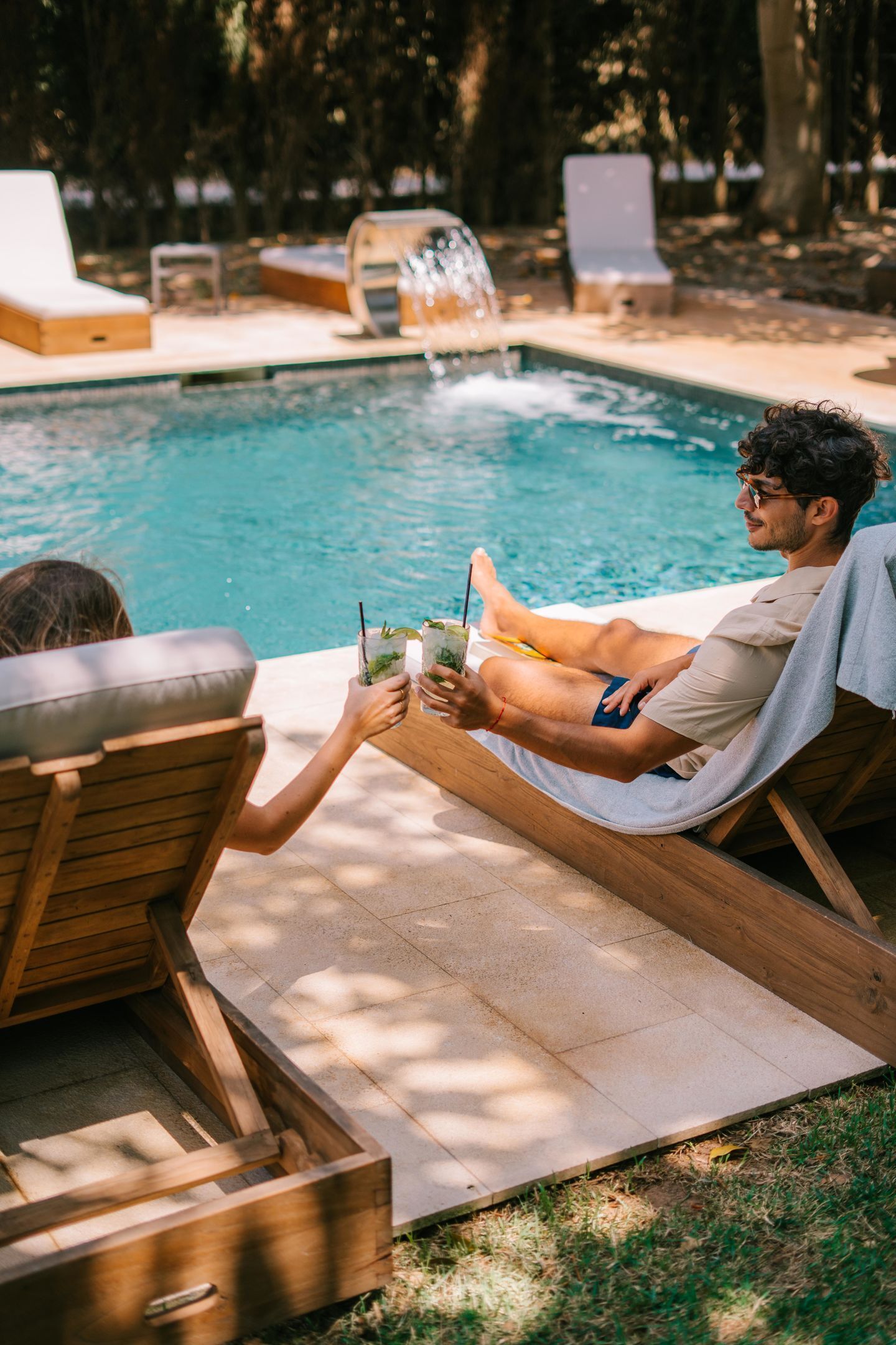 Un espace aménagé au bord de la piscine, avec des chaises longues en bois et une petite cascade décorative.