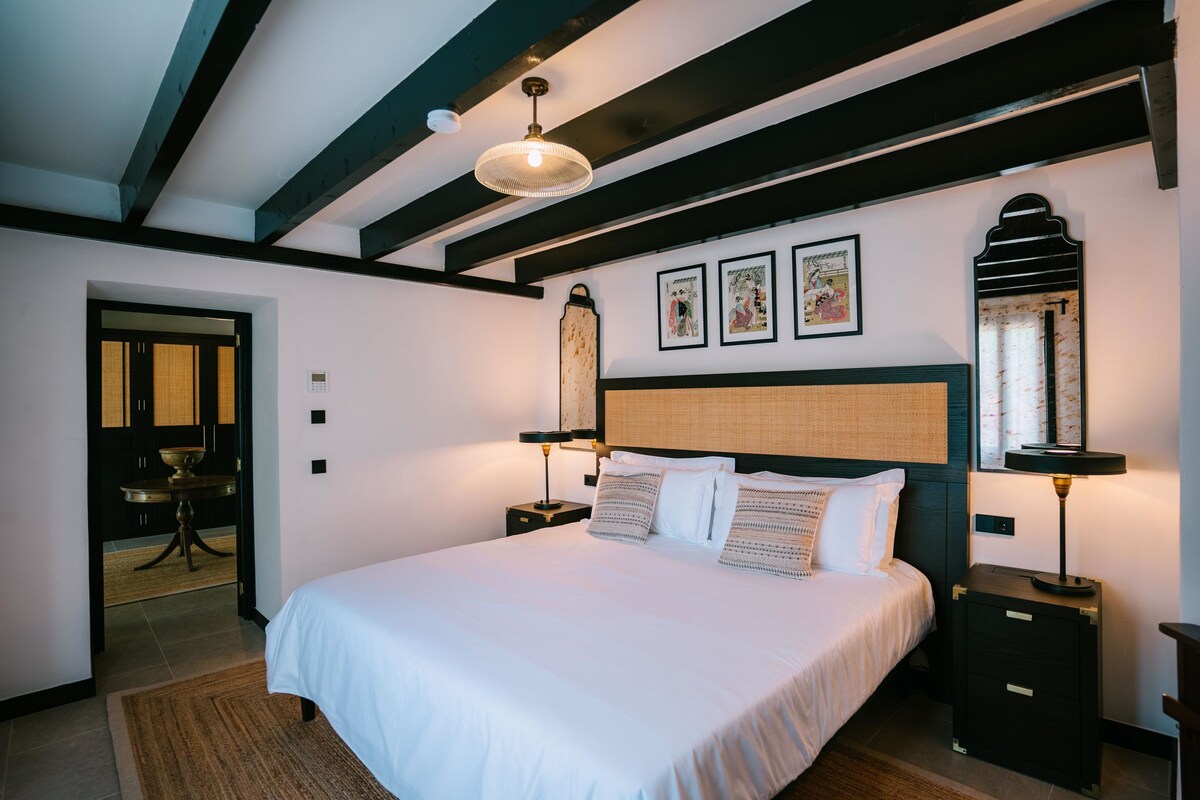 Een slaapkamer met een groot bed, nachtkastjes, een hanglamp en kunstwerken aan de muren.