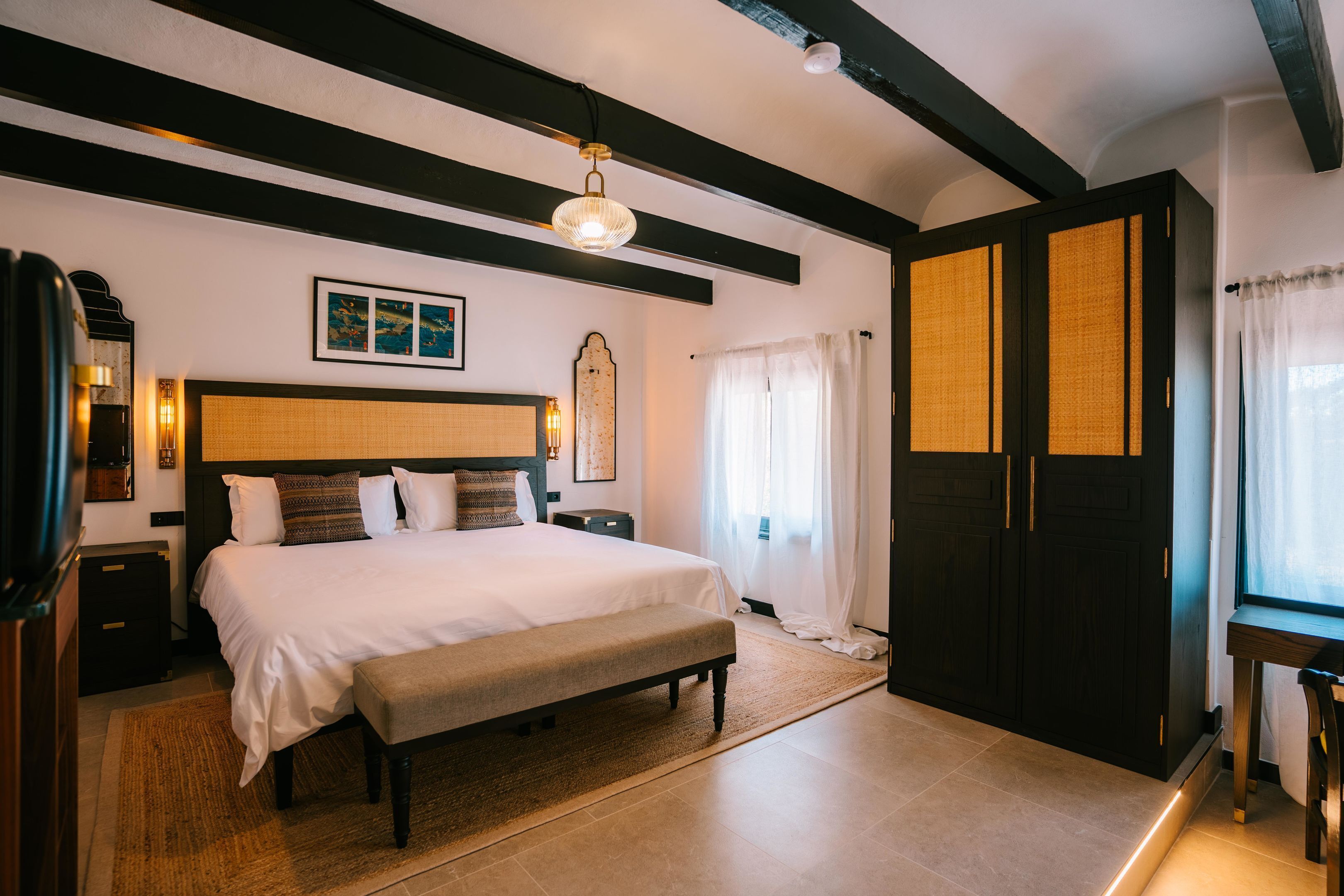 Une chambre à coucher avec un grand lit, un banc, une table de chevet, une armoire et un luminaire au plafond.