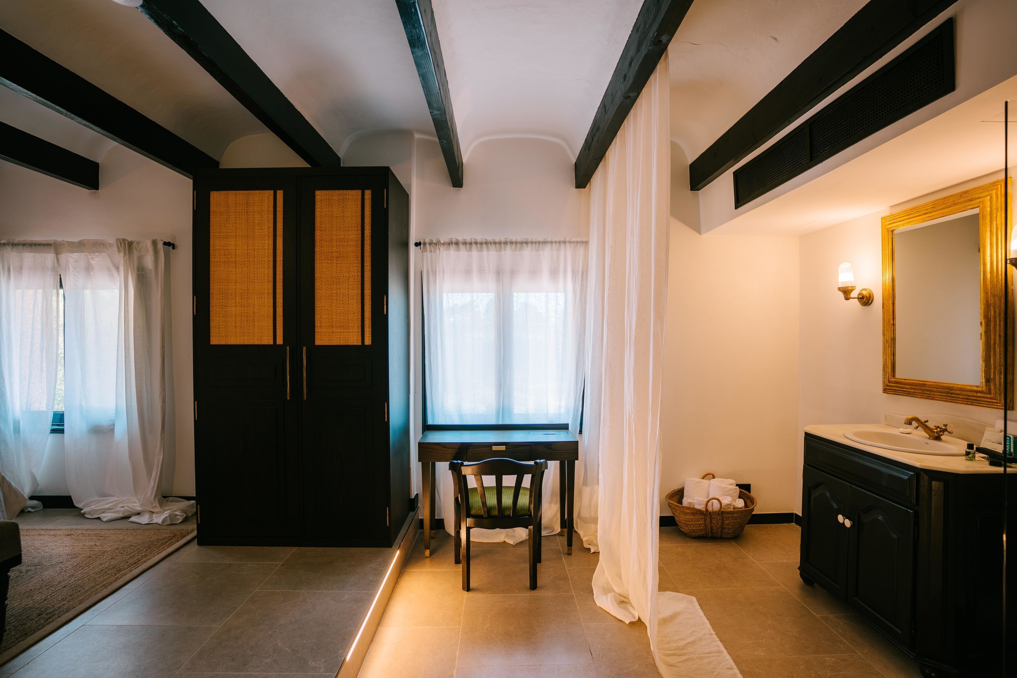 Een kamer met een bed, een bureau, een stoel, een kledingkast, een badkamer met een wastafel en spiegel, en een raam met gordijnen.