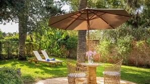 A circular stone patio with wicker furniture, including two chairs and a table, under a large umbrella.