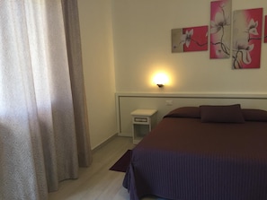 Una camera da letto con un letto, tende, un comodino, una lampada a muro e un'opera d'arte floreale.