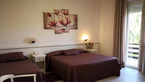 A hotel room with two beds, a white chair, a nightstand with a lamp, and a wall-mounted painting. - Albergo Ester Di Fossi Laura (Rimini)