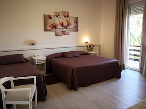 Una camera d'albergo con due letti, una sedia bianca, un comodino con lampada e un quadro appeso al muro.