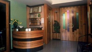 A reception area with a wooden reception desk, framed certificates on the wall, and a door with frosted glass panels. - Albergo Ester di Fossi Laura (Rimini)