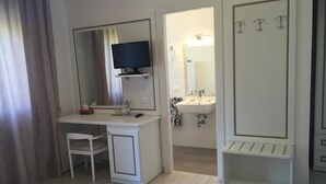 A hotel room with a desk, chair, TV, and a bathroom with a sink and mirror. - Albergo Ester di Fossi Laura (Rimini)
