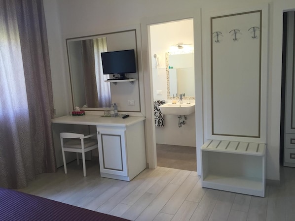 Una camera d'albergo con scrivania, sedia, televisore e bagno completo di lavabo e specchio.