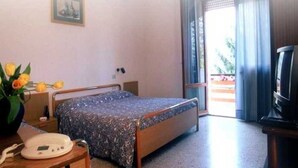 A hotel room with a bed, a bedside table with a lamp, a telephone, a TV, and a window with curtains. - Albergo Ester Di Fossi Laura (Rimini)