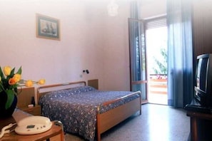 Una camera d'albergo con un letto, un comodino con una lampada, un telefono, una TV e una finestra con tende.