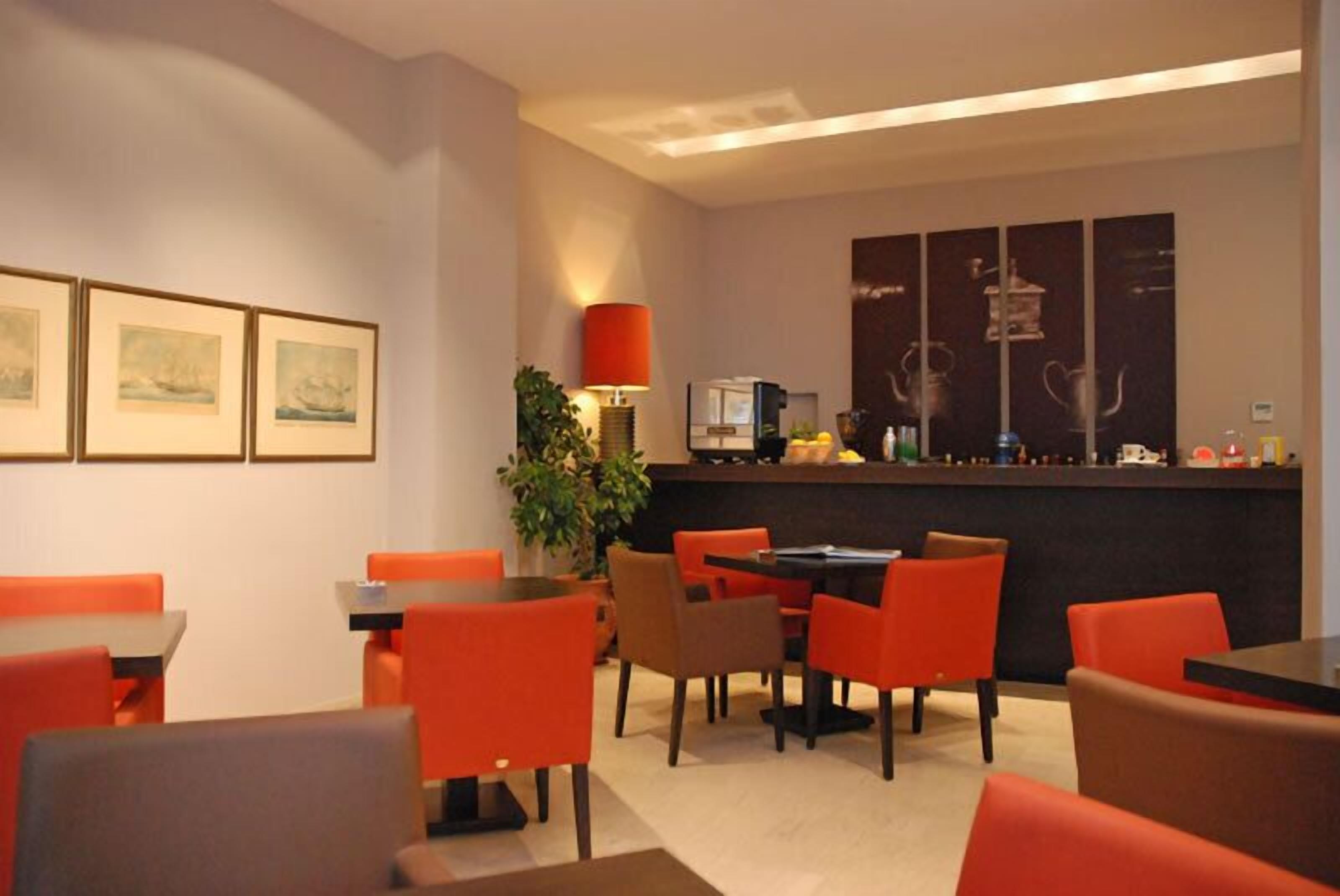 A modern restaurant with orange chairs and tables, a counter with a red lamp, and framed artwork on the walls.