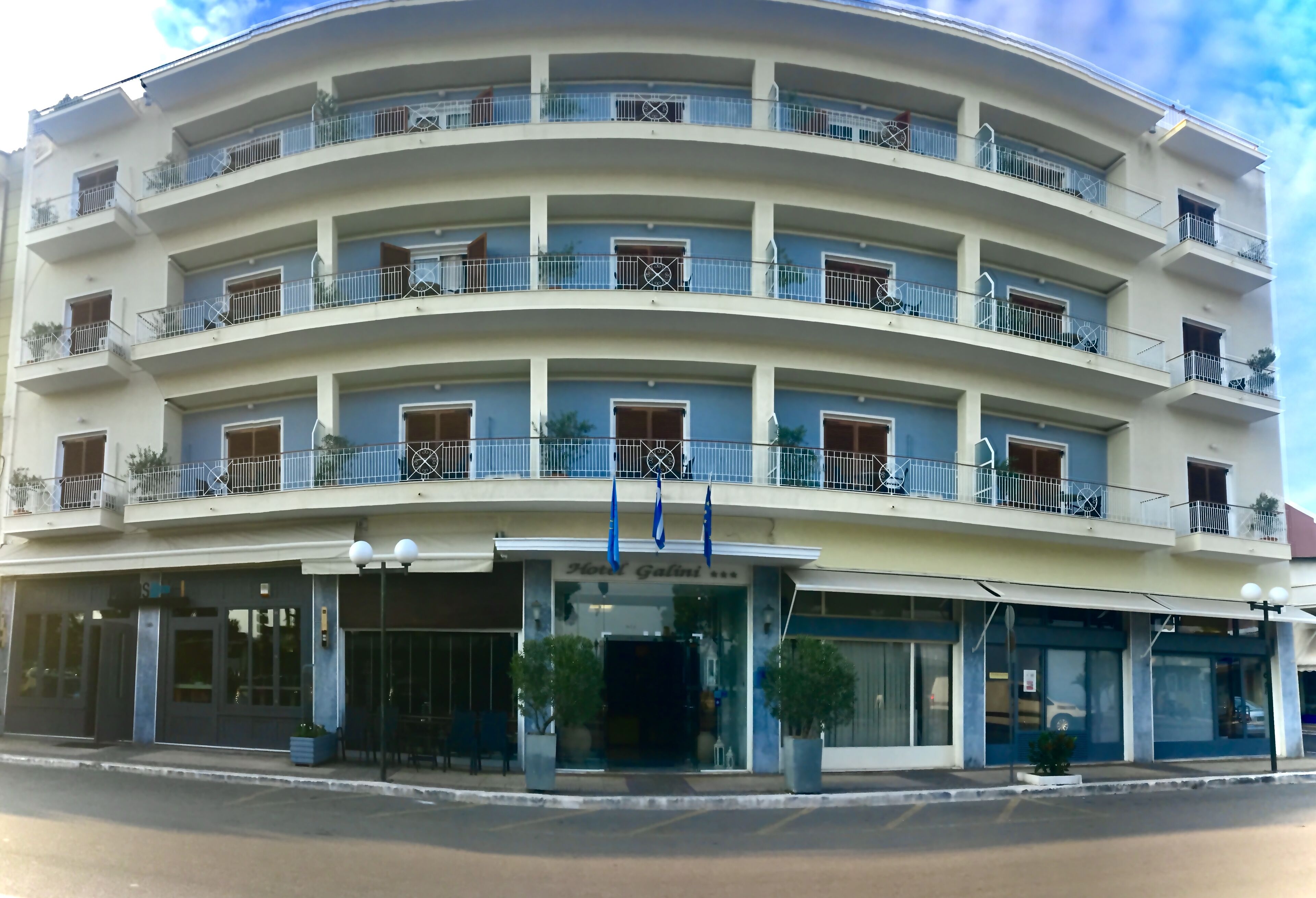A multi-story hotel with balconies, a central entrance, and potted plants.