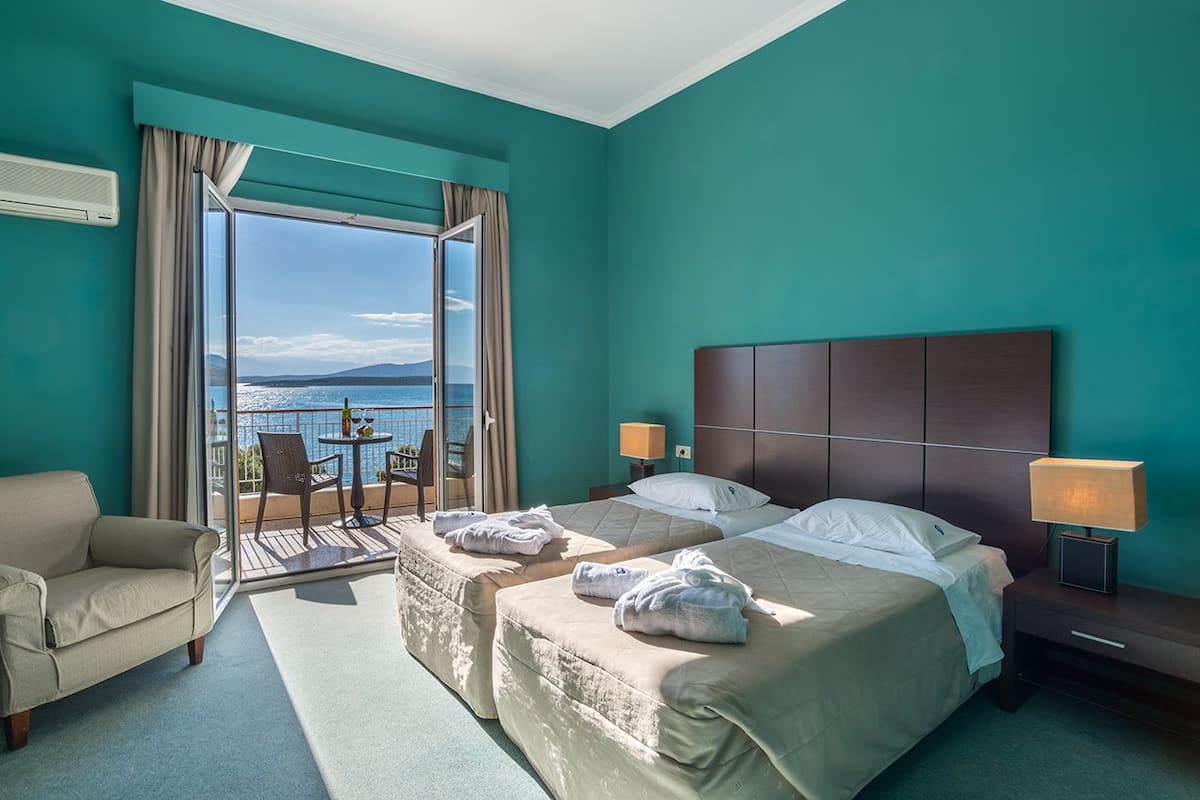 A hotel room with two beds, a sofa, a balcony with a table and chairs, and a view of the sea.