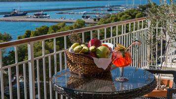 Un balcón con una cesta de mimbre llena de fruta, un vaso de bebida y vistas a un puerto deportivo y al agua.