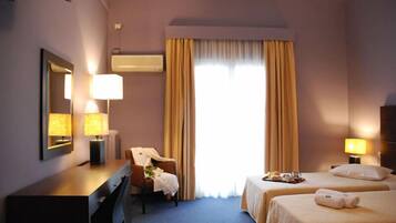 Ein Hotelzimmer mit Schreibtisch, zwei Betten, einem Sessel und einem großen Fenster mit Vorhängen.