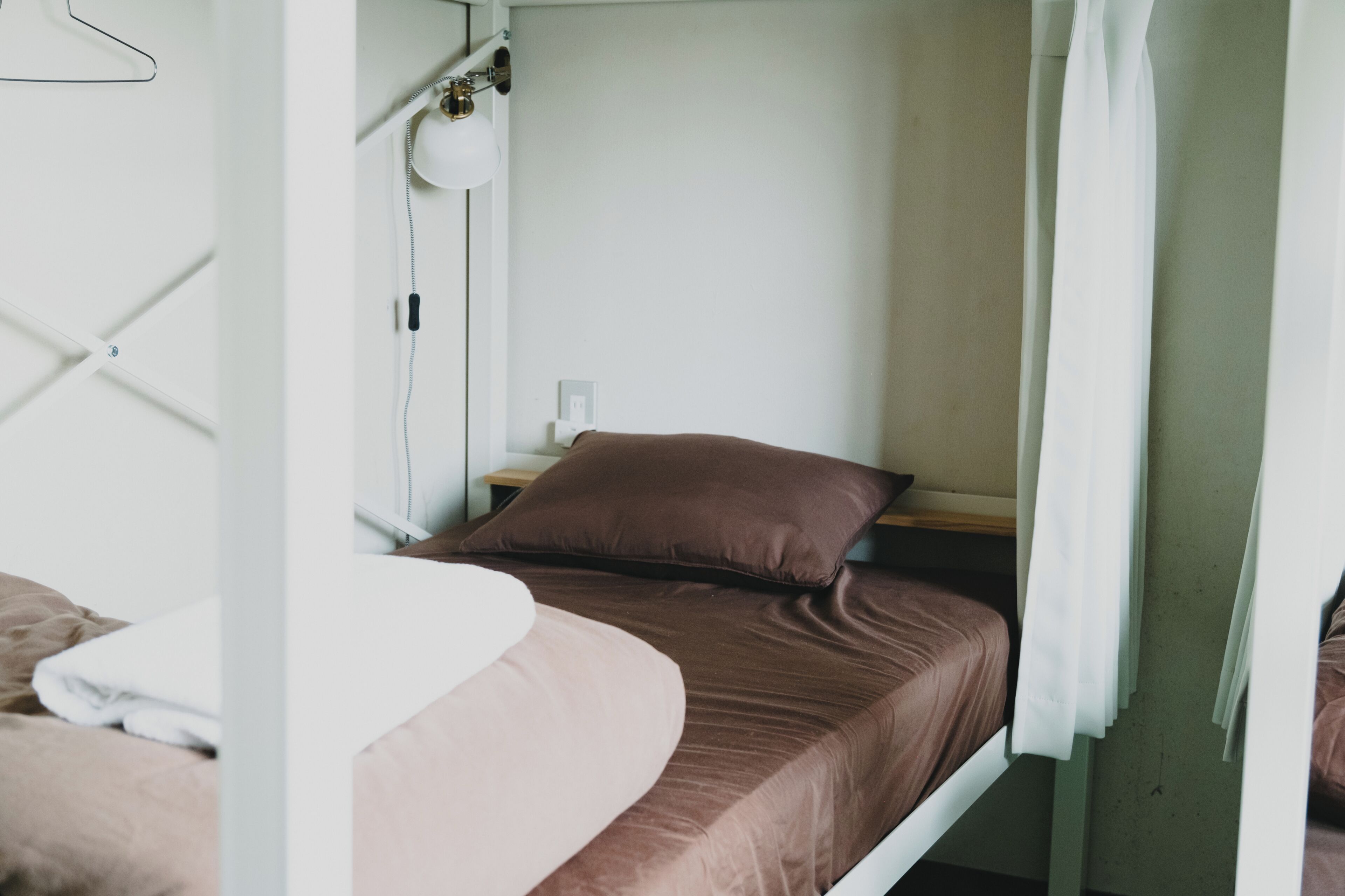 Una cama litera con cabecera blanca, una lámpara de noche y una almohada marrón.