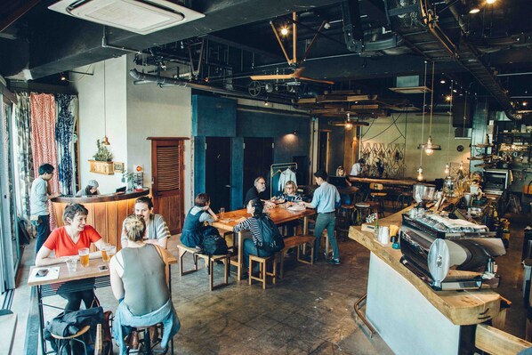 A café with wooden tables and chairs, a coffee machine, and a counter where staff are serving. - Len KYOTO KAWARAMACHI – Hostel (Kyoto)