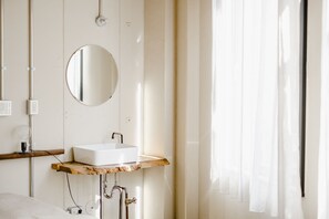 A bathroom with a white sink on a wooden countertop, a round mirror, and a shower area. - Len KYOTO KAWARAMACHI – Hostel (Kyoto)