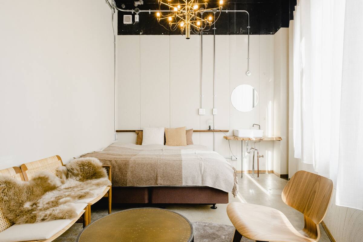 A modern bedroom with a large bed, a round mirror, a wooden chair, and a small table.