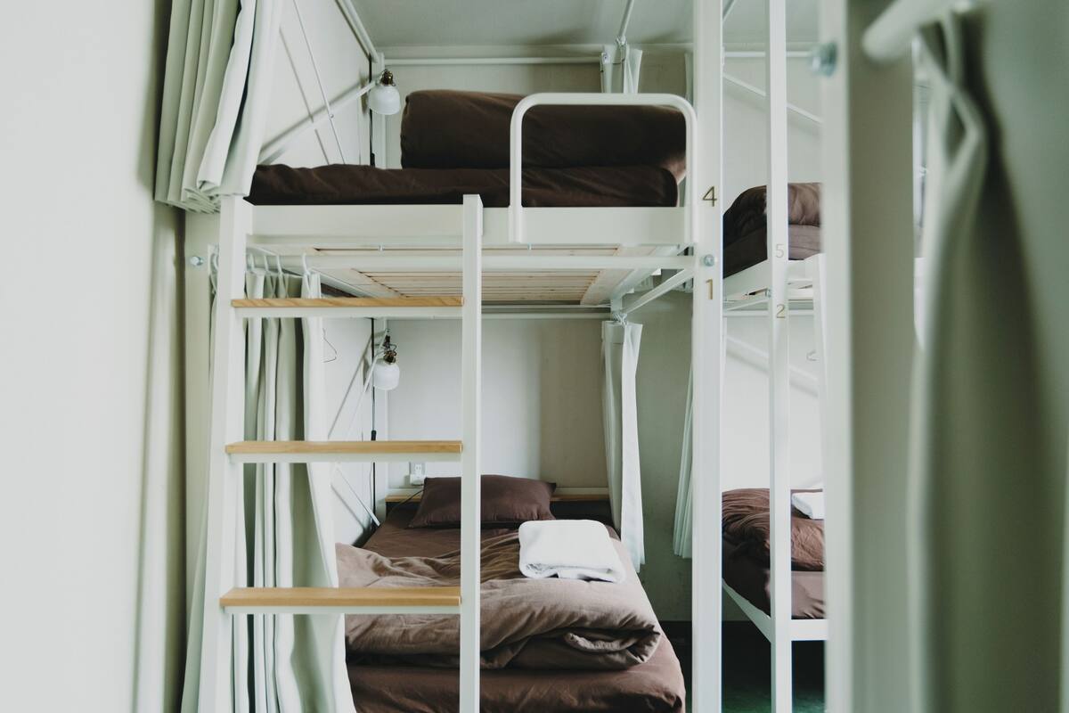 A bunk bed room with a ladder, a window with curtains, and a bedside table with a lamp.