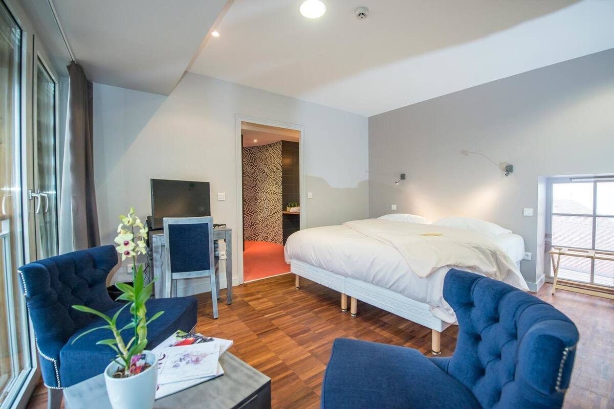 Une chambre d’hôtel moderne avec un grand lit, un bureau avec une chaise, une plante en pot et une vue sur l’extérieur.