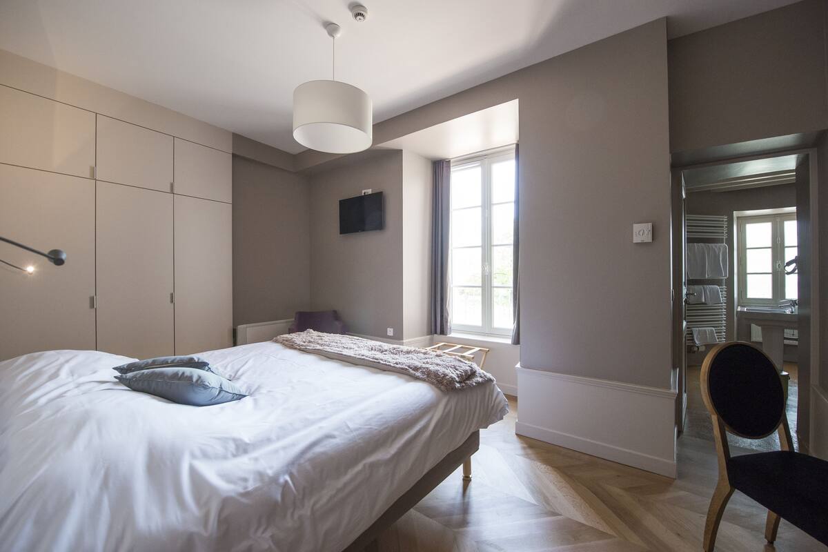 Une chambre à coucher avec un lit, une chaise, une télévision et une fenêtre.
