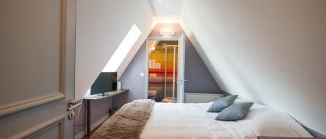 A bedroom with a sloped ceiling, a bed with pillows, a bedside table, and a TV.