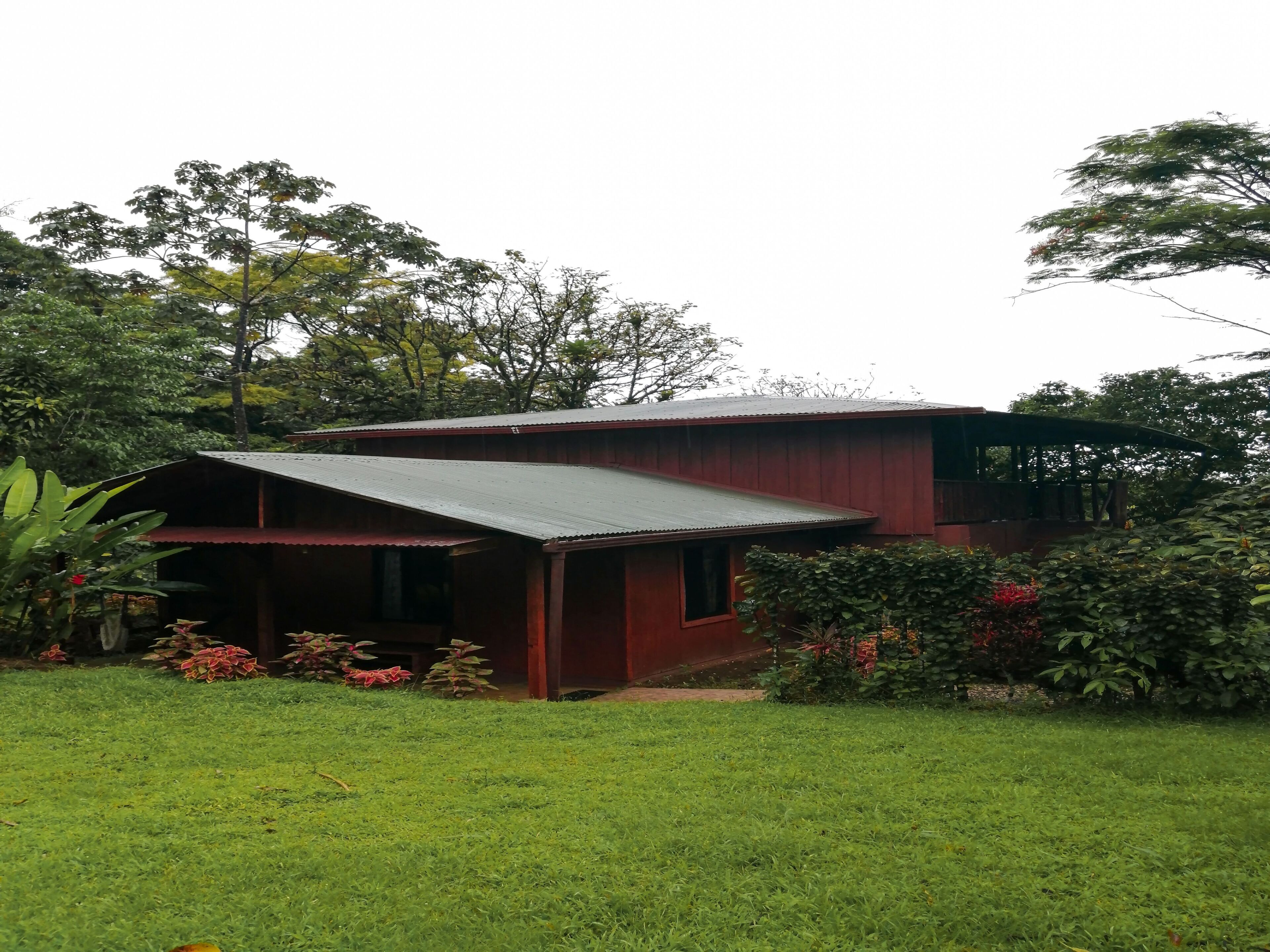 Un bâtiment à deux étages, à la façade rouge, entouré d’une végétation luxuriante et d’une pelouse bien entretenue.