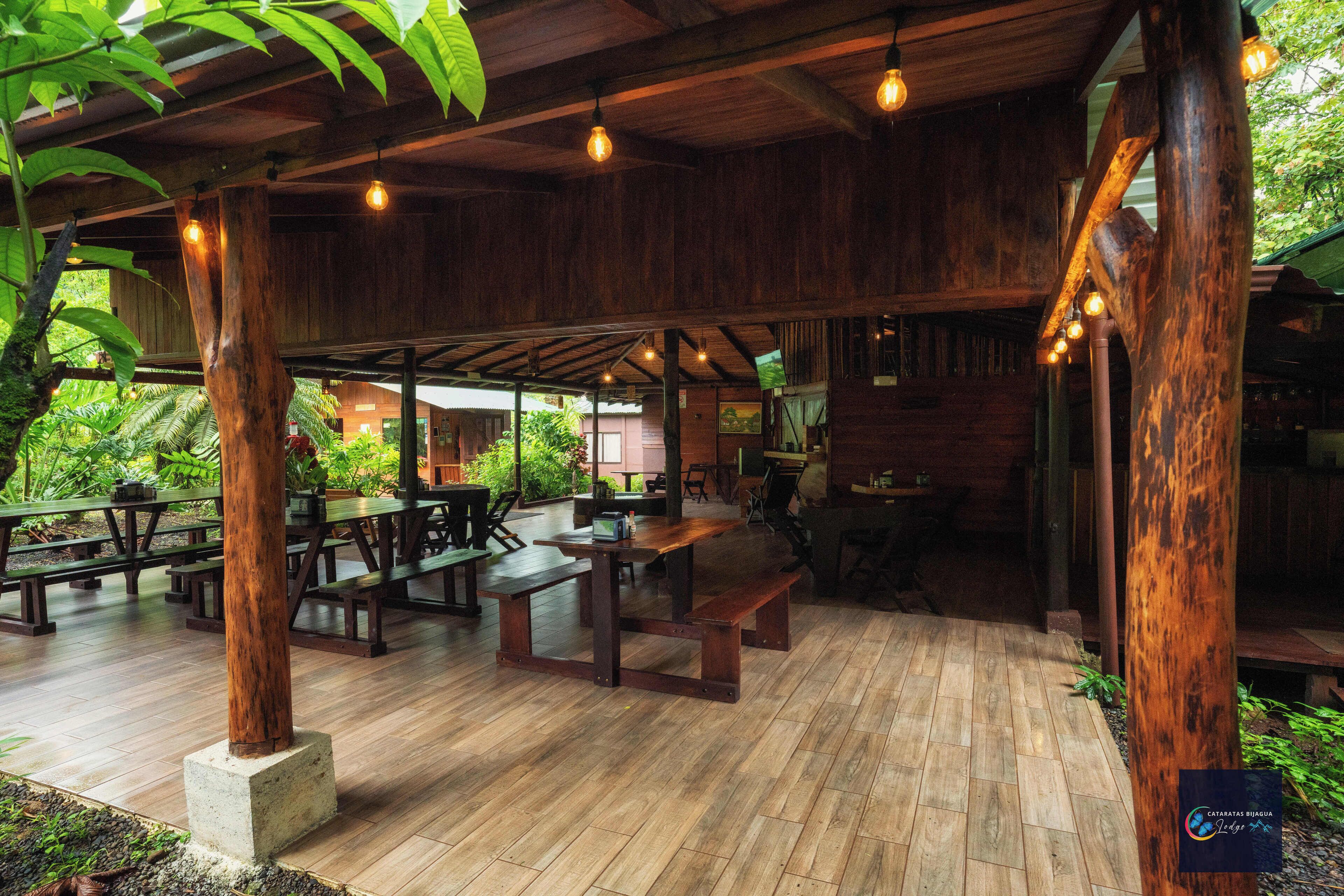 Um pavilhão de madeira ao ar livre, com mesas e bancos de piquenique, rodeado por vegetação.